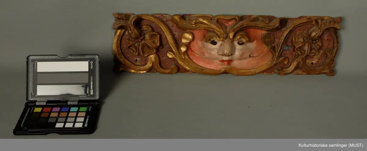 I midten en faunmaske, hvorfra utgår til begge sider en rankegren.
