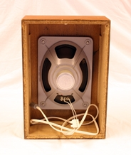 Høytaler. Rektangulær. Treverk. Teakfiner. Mangler bakside. Selve høytaleren festet på innersiden. Den er rektangulær med ovalformet forhøyning. Metall. Ledning festet til forhøyning. Forhøyningen har et åpent felt med tekstil. Fronten har langsgående riller.