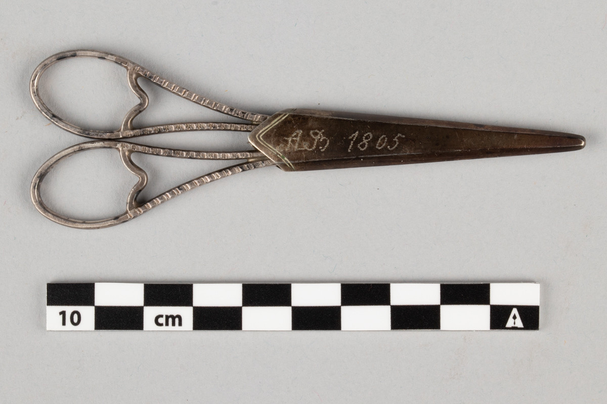 Liten saks for sying og brodering. Saksen har et etui med inngravert initialene til Anne Marlene Bruun og årstallet 1805