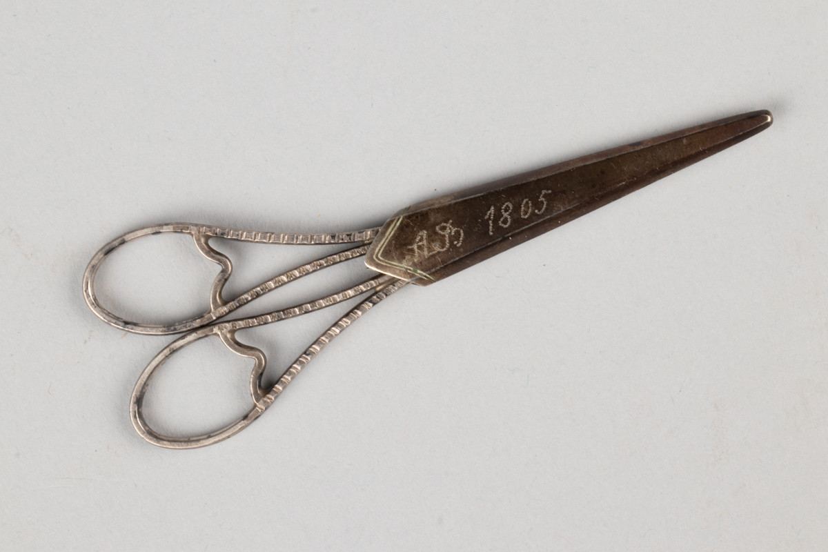 Liten saks for sying og brodering. Saksen har et etui med inngravert initialene til Anne Marlene Bruun og årstallet 1805