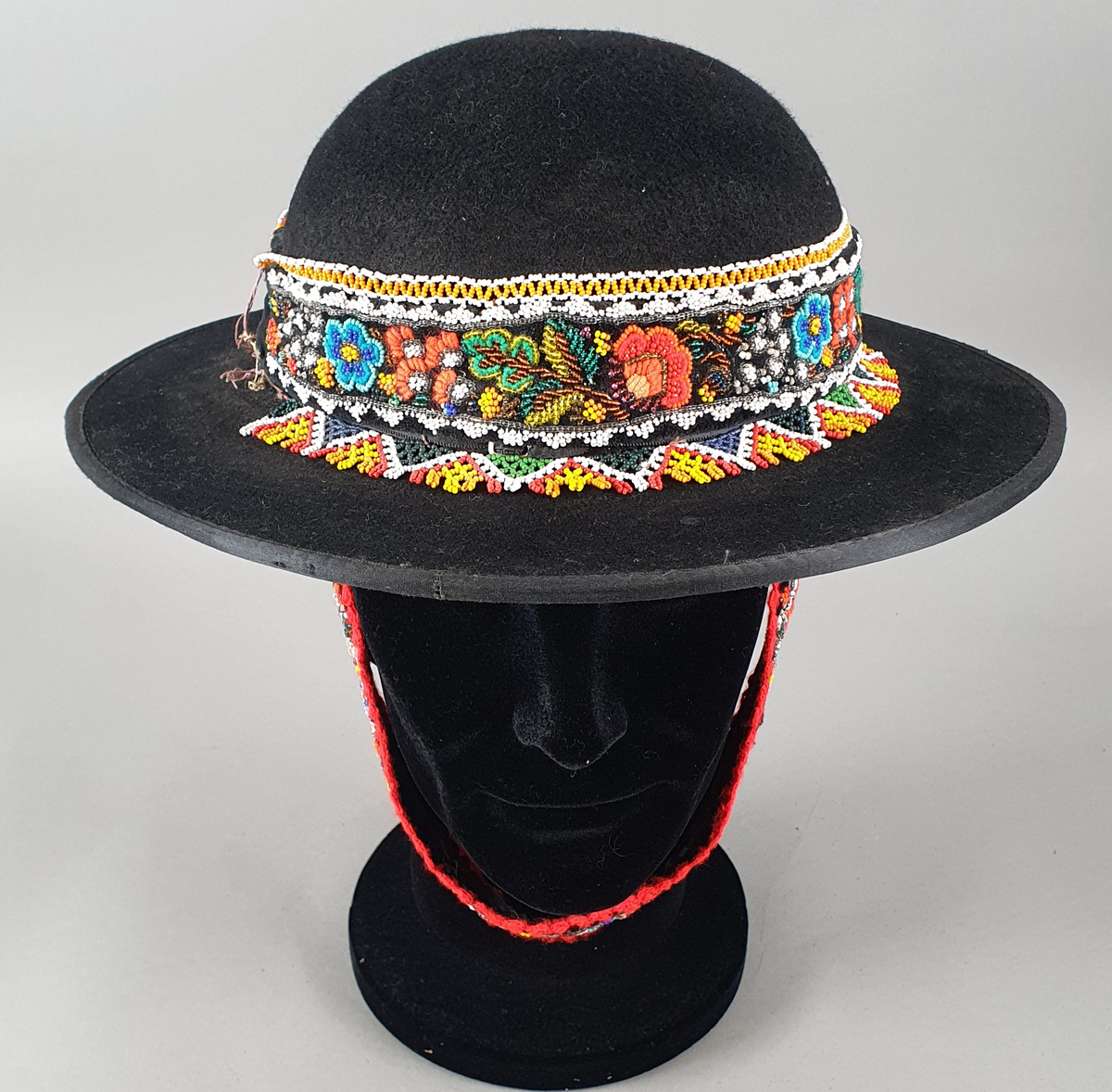 Svart hatt av filt med perlebroderi rundt pullen. Bred brem. Perlebrodert bånd til å feste under haken.