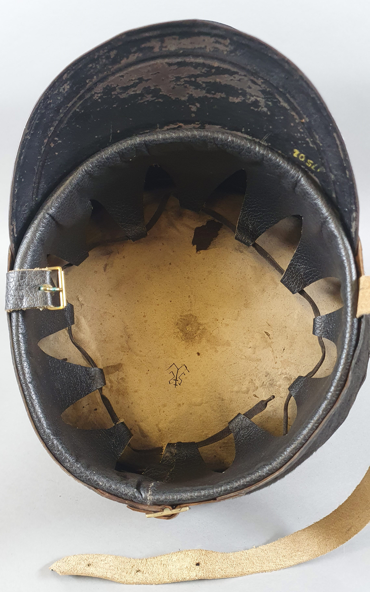 Militærhatt med svart plysjtrekk på pullen som har konisk form- bredest øverst. Rosett med gullenke og riksvåpen midt foran. Svart skygge og svart skinnreim rundt pullen nederst, festet med spenne midt bak. Reim under haken med spenne på høyre side. Skinn på innsiden med snor som kan strammes.