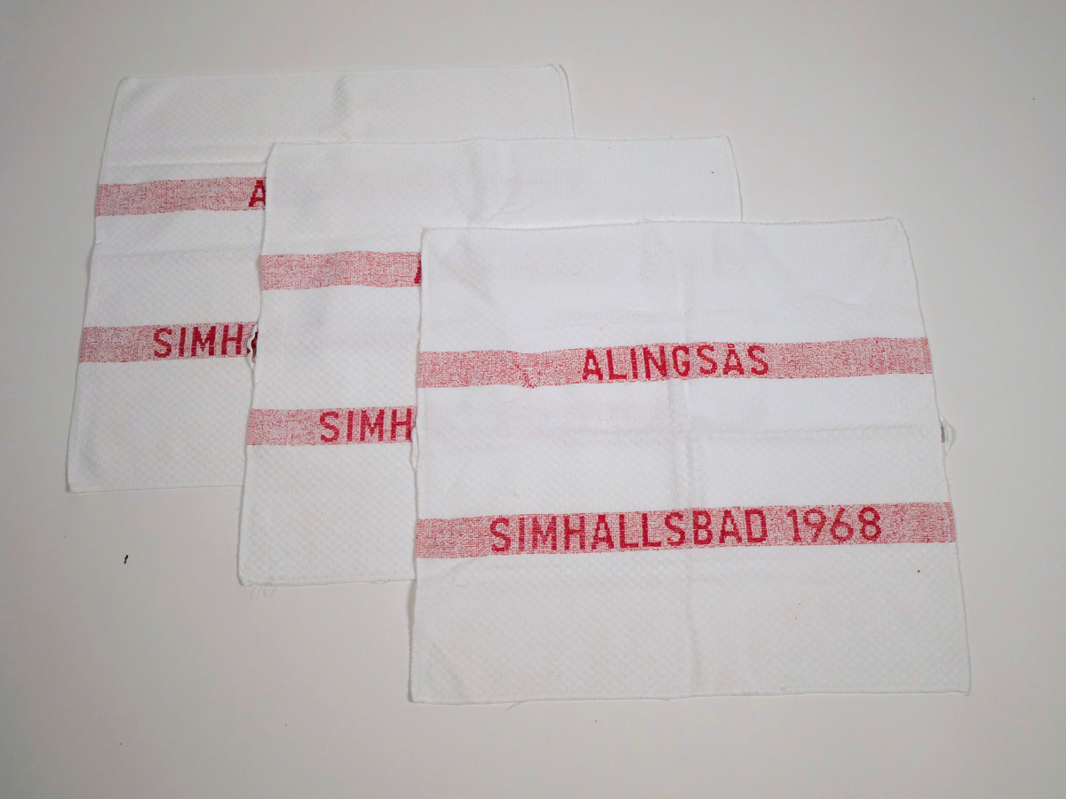 Små vita frottéhanddukar med röd text "ALINGSÅS SIMHALLSBAD 1968"