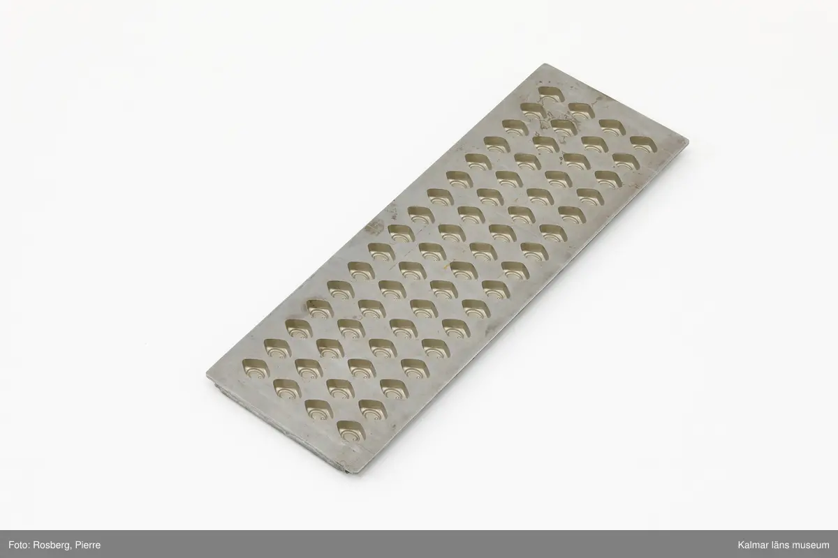 KLM 39470:200 Form, chokladform. Grå metallplåt, stål, med flera små fyrhörniga formar med mönster, för gjutning av chokladpraliner. Stämpel baksida: 9 VORMEN FABRIEK TILBURG-HOLLAND 69 P4304.