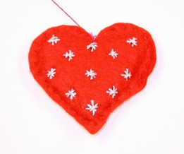 Julepynt. Filthjerte. Fylt. Tråklet sammen. Tråd til oppheng i hjertegropa. Broderte sølvstjerner på den ene siden. Stearinlys i gulltråd på motsatt side.