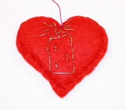 Julepynt. Filthjerte. Fylt. Tråklet sammen. Tråd til oppheng i hjertegropa. Broderte sølvstjerner på den ene siden. Stearinlys i gulltråd på motsatt side.