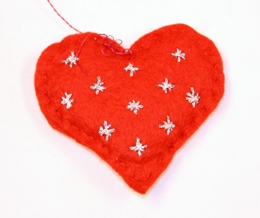 Julepynt. Filthjerte. Fylt. Tråklet sammen. Tråd til oppheng i hjertegropa. Stjerner brodert med sølvtråd på dene ene siden. 3 stjerner brodert med gulltråd på motsatt side.
