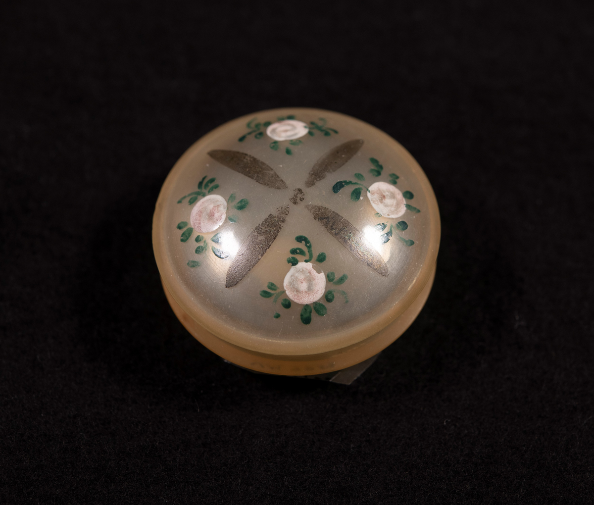Svarvad av horn (tunnt som celluloid), med kupigt lock och botten. På locket målade rosor.