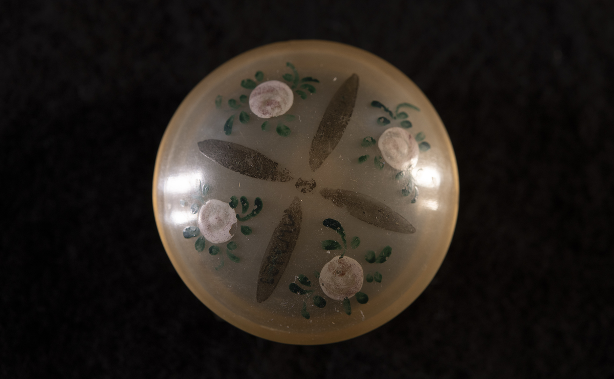 Svarvad av horn (tunnt som celluloid), med kupigt lock och botten. På locket målade rosor.