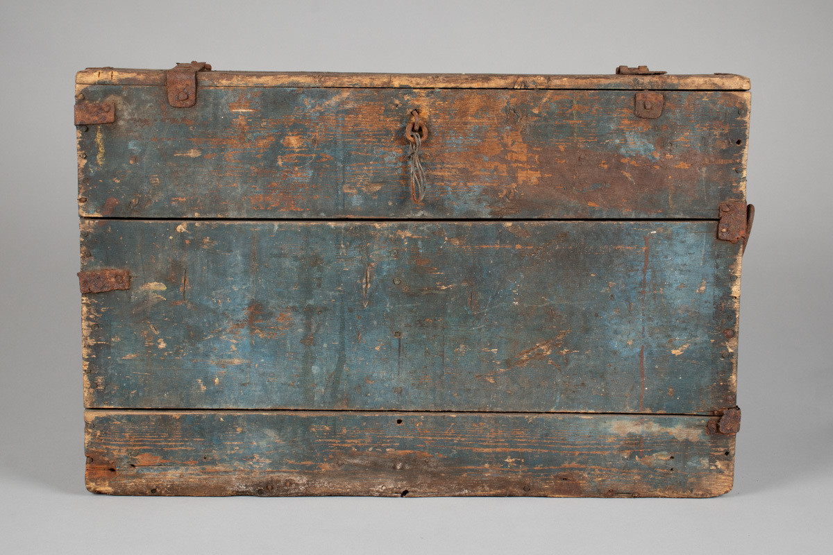 Håndhøvlet, malt og utskjært kiste i tre med jernbeslag og hektelås. Inne i kista er der tre rom, to store, og en liten skuff som har løsnet  på den ene siden.