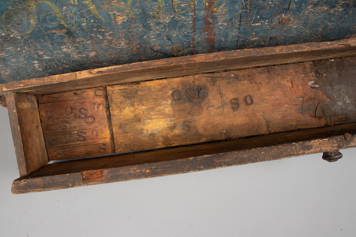 Håndhøvlet, malt og utskjært kiste i tre med jernbeslag og hektelås. Inne i kista er der tre rom, to store, og en liten skuff som har løsnet  på den ene siden.