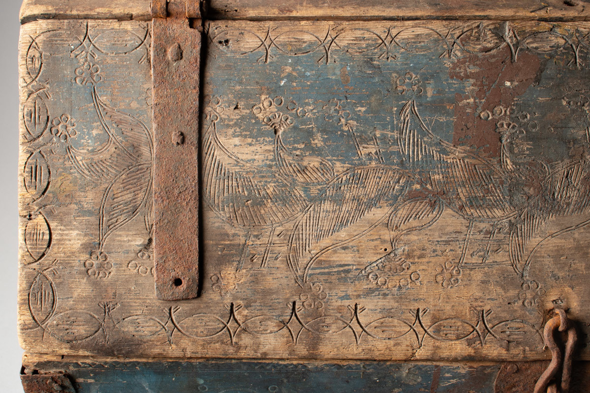 Håndhøvlet, malt og utskjært kiste i tre med jernbeslag og hektelås. Inne i kista er der tre rom, to store, og en liten skuff som har løsnet  på den ene siden.