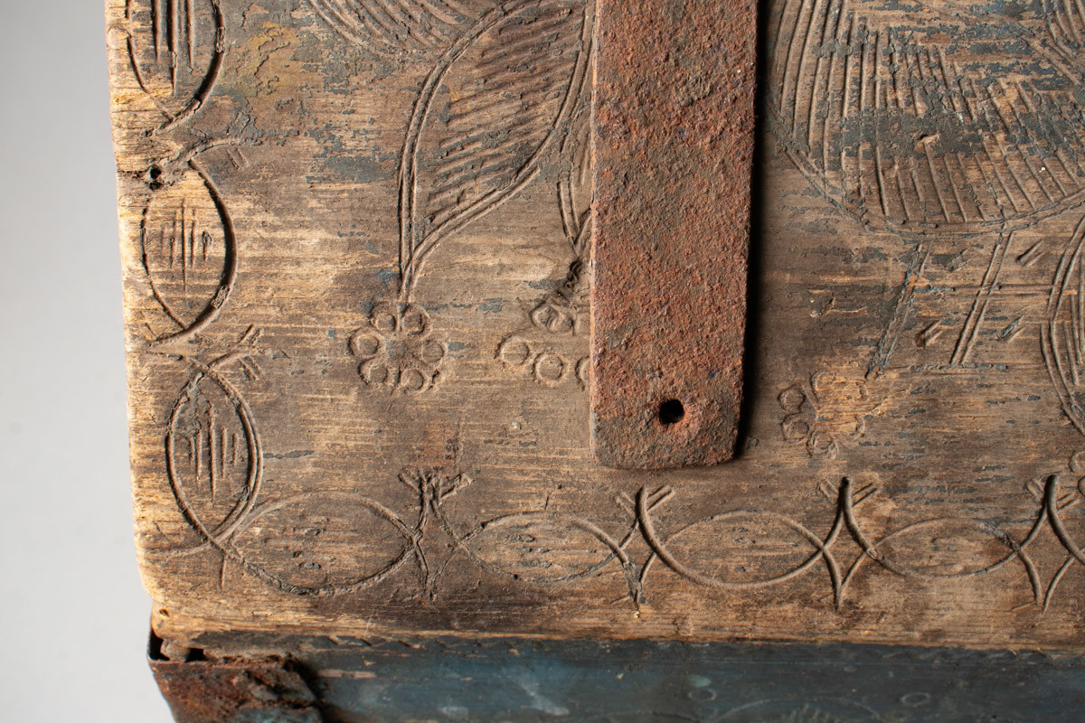 Håndhøvlet, malt og utskjært kiste i tre med jernbeslag og hektelås. Inne i kista er der tre rom, to store, og en liten skuff som har løsnet  på den ene siden.