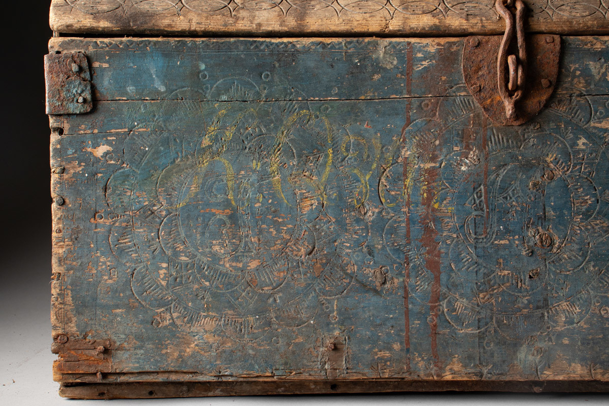 Håndhøvlet, malt og utskjært kiste i tre med jernbeslag og hektelås. Inne i kista er der tre rom, to store, og en liten skuff som har løsnet  på den ene siden.