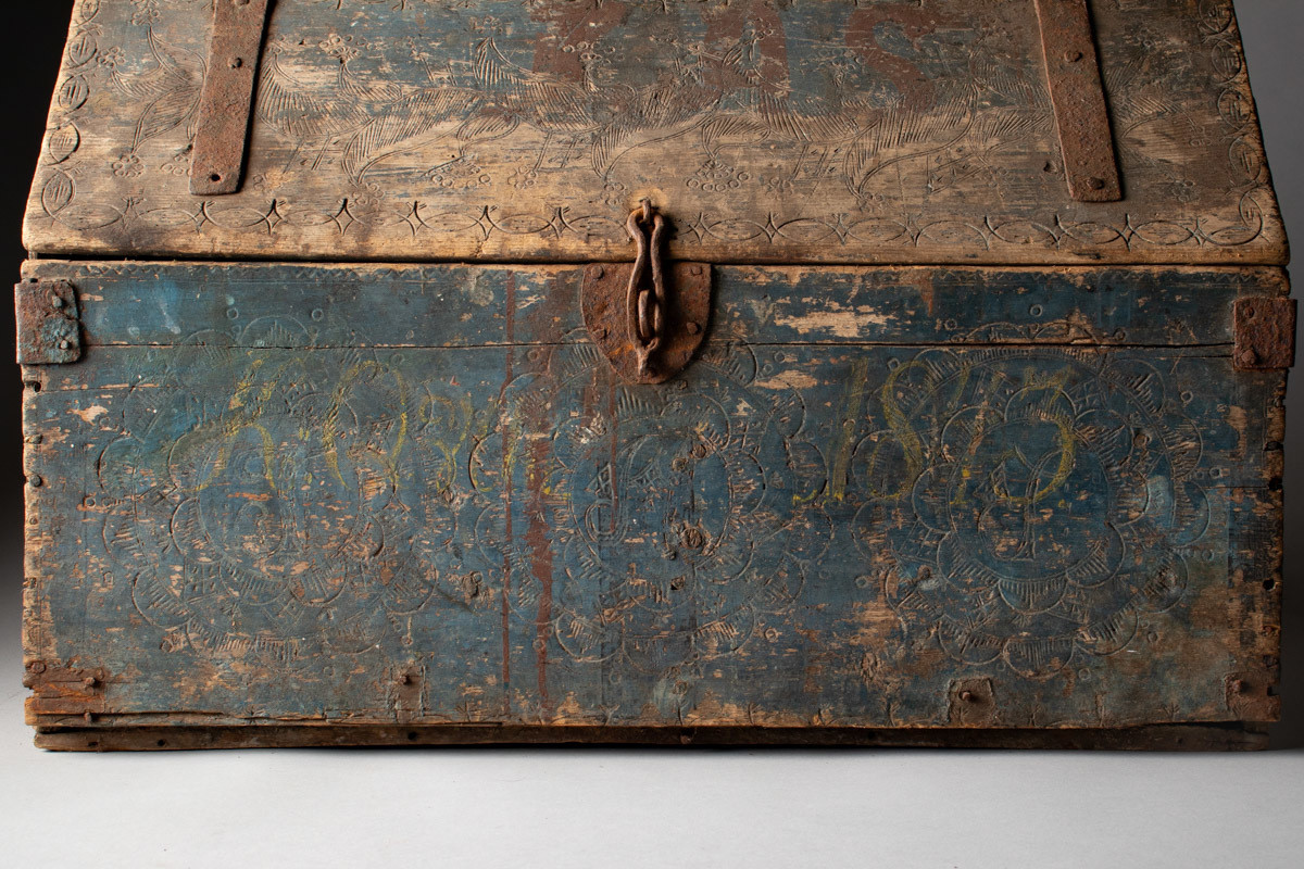 Håndhøvlet, malt og utskjært kiste i tre med jernbeslag og hektelås. Inne i kista er der tre rom, to store, og en liten skuff som har løsnet  på den ene siden.