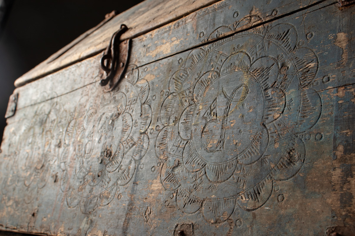 Håndhøvlet, malt og utskjært kiste i tre med jernbeslag og hektelås. Inne i kista er der tre rom, to store, og en liten skuff som har løsnet  på den ene siden.