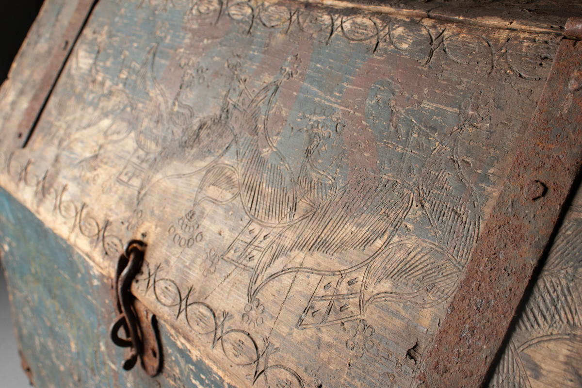 Håndhøvlet, malt og utskjært kiste i tre med jernbeslag og hektelås. Inne i kista er der tre rom, to store, og en liten skuff som har løsnet  på den ene siden.