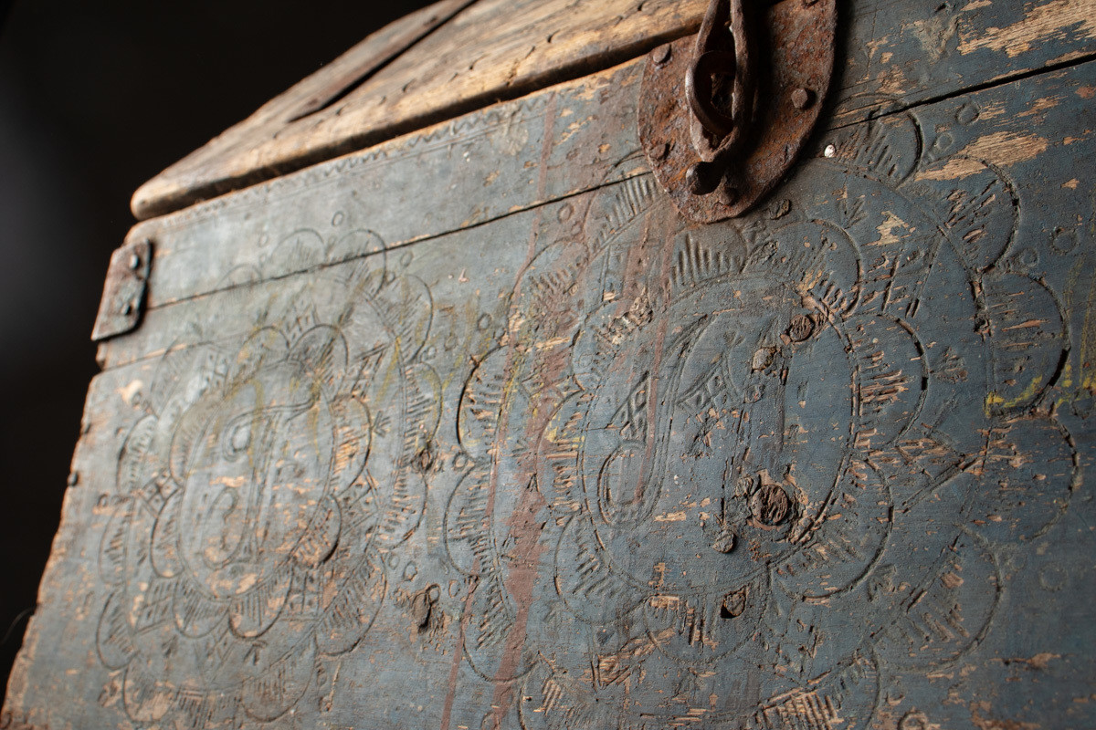 Håndhøvlet, malt og utskjært kiste i tre med jernbeslag og hektelås. Inne i kista er der tre rom, to store, og en liten skuff som har løsnet  på den ene siden.