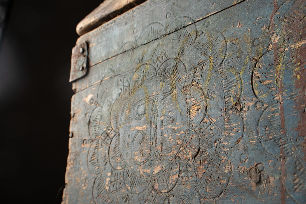 Håndhøvlet, malt og utskjært kiste i tre med jernbeslag og hektelås. Inne i kista er der tre rom, to store, og en liten skuff som har løsnet  på den ene siden.