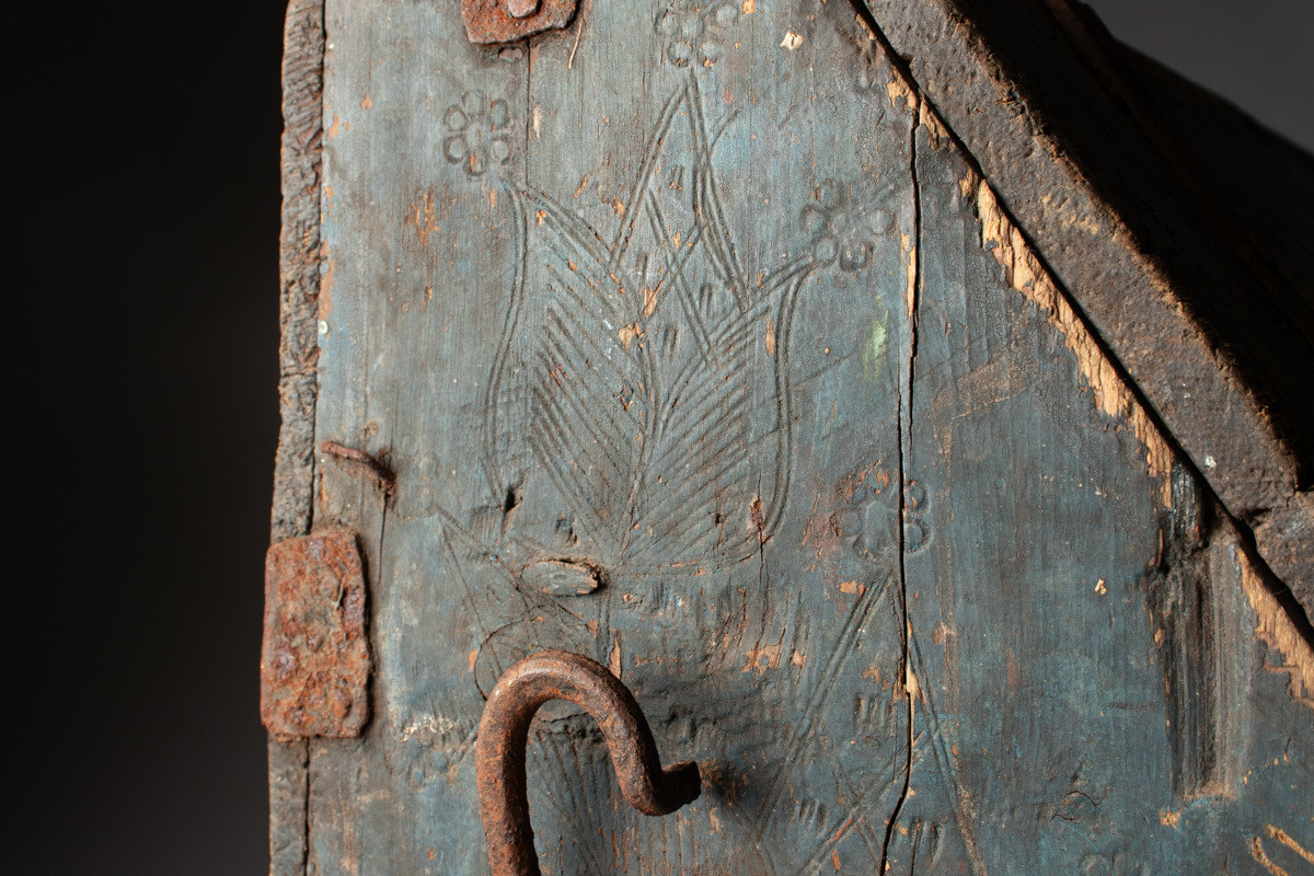 Håndhøvlet, malt og utskjært kiste i tre med jernbeslag og hektelås. Inne i kista er der tre rom, to store, og en liten skuff som har løsnet  på den ene siden.