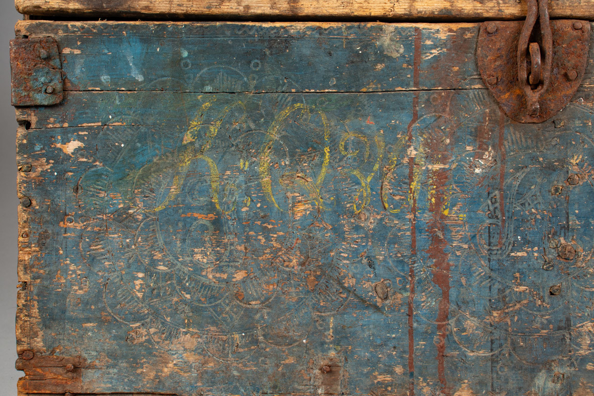 Håndhøvlet, malt og utskjært kiste i tre med jernbeslag og hektelås. Inne i kista er der tre rom, to store, og en liten skuff som har løsnet  på den ene siden.