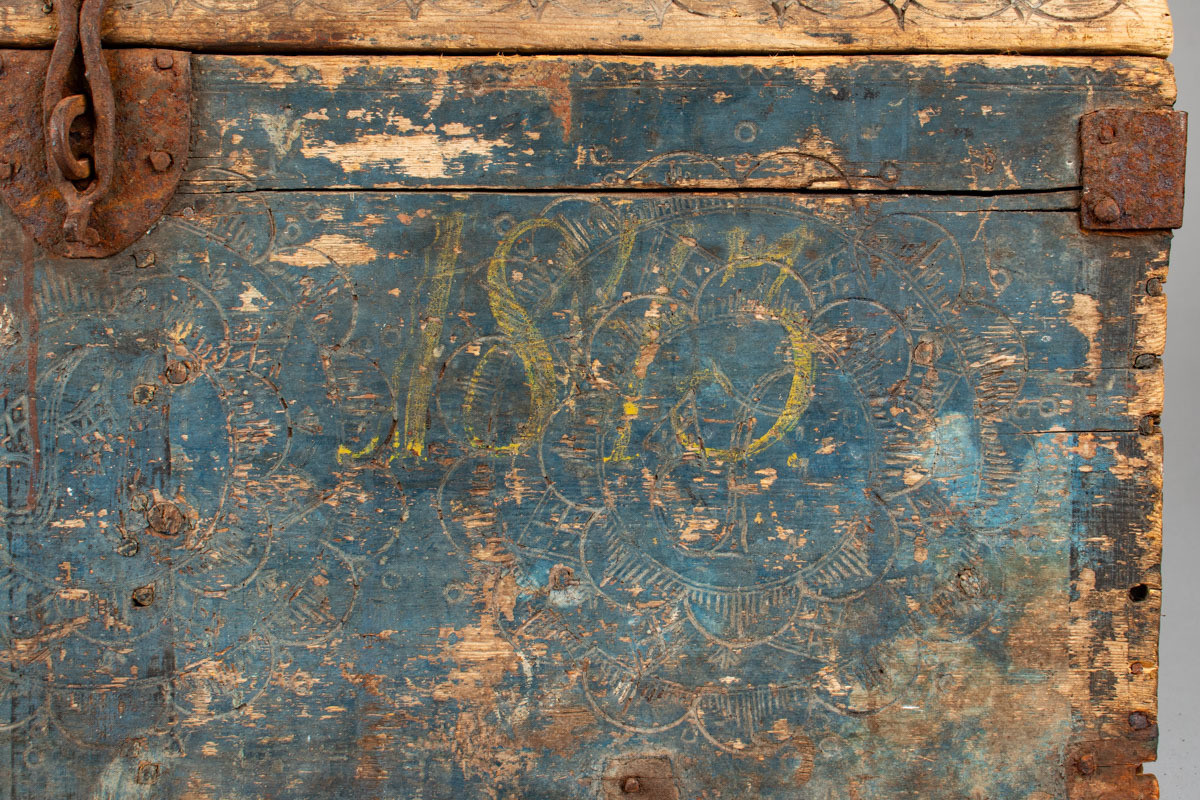 Håndhøvlet, malt og utskjært kiste i tre med jernbeslag og hektelås. Inne i kista er der tre rom, to store, og en liten skuff som har løsnet  på den ene siden.