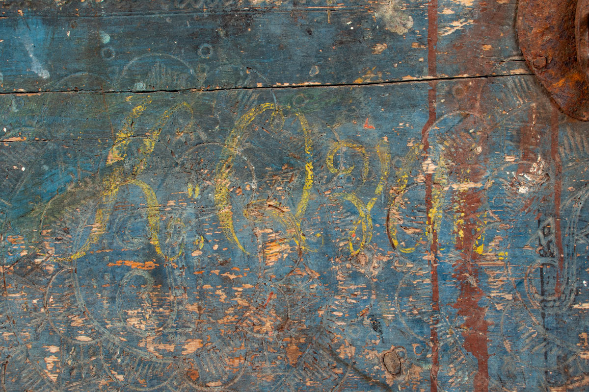 Håndhøvlet, malt og utskjært kiste i tre med jernbeslag og hektelås. Inne i kista er der tre rom, to store, og en liten skuff som har løsnet  på den ene siden.