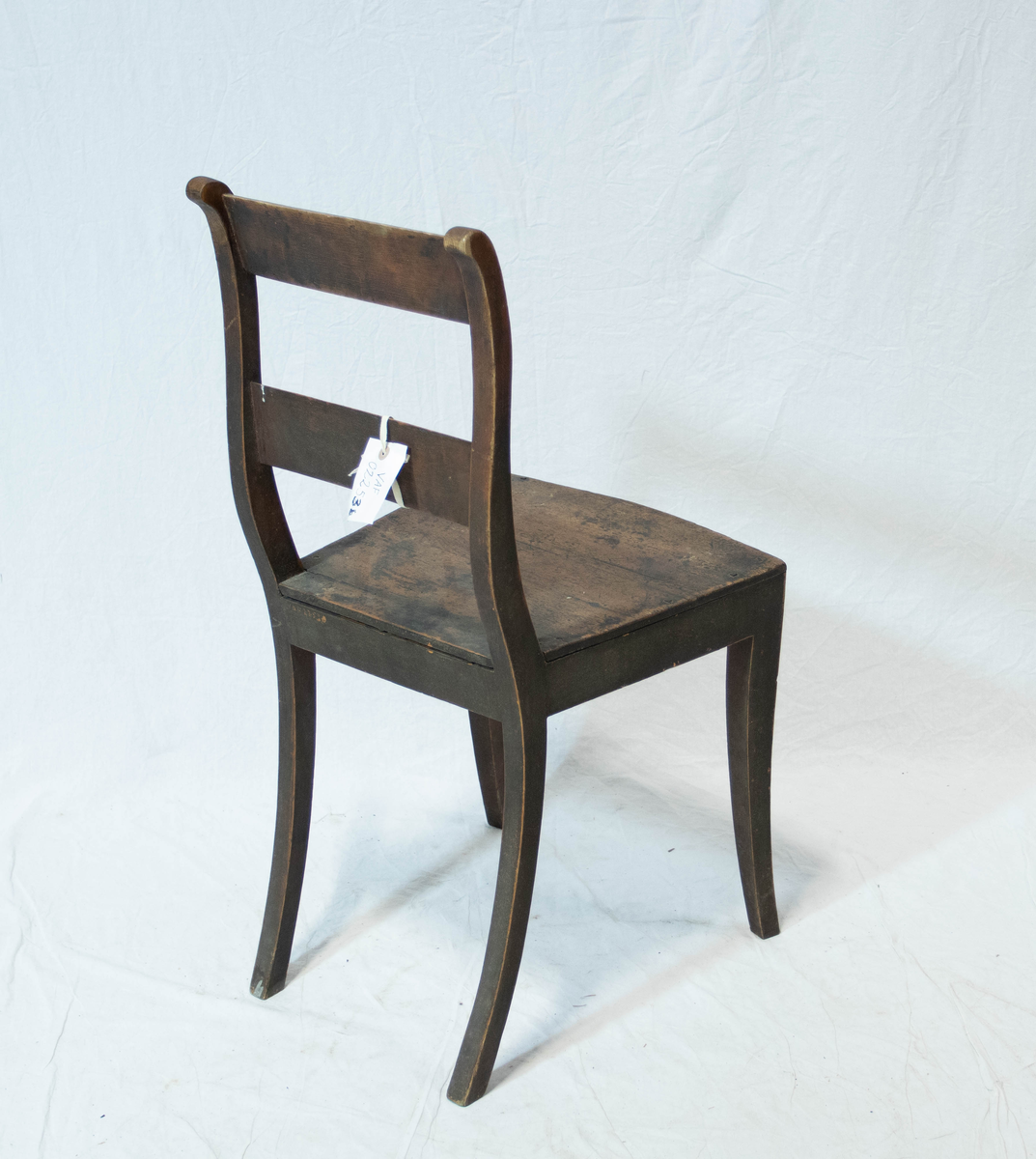 Stol av tre. Stolen har fire sabelformede ben og glatt sarg. Setet er trapeslignende med horisontalt buet fremkant.  Stolen har S-svungne ryggstaver forbundet med to glatte horisontale bretter.