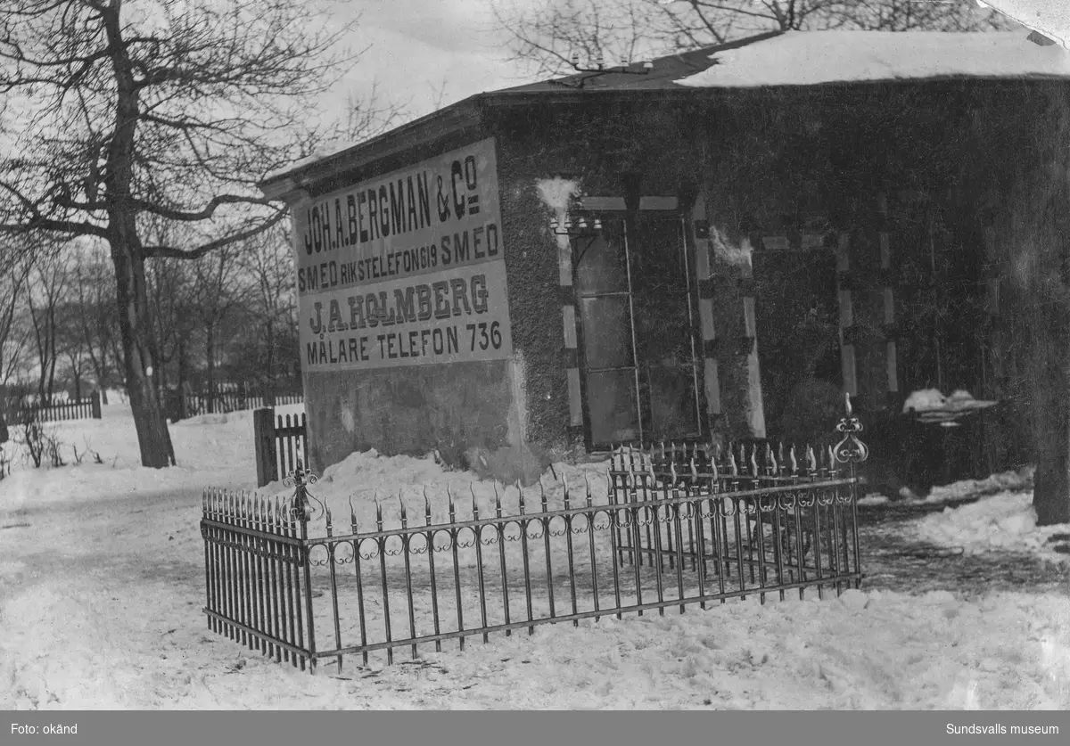 Smidesmästare Johan August Bergmans (1870–1954) mekaniska verkstad på tomten där Centralstationen senare byggdes (klar 1926). Ett vackert utsirat smitt staket står framför den lilla byggnaden. Skyltat även för målare J.A. Holmberg. Ur Anders Nylanders samling.