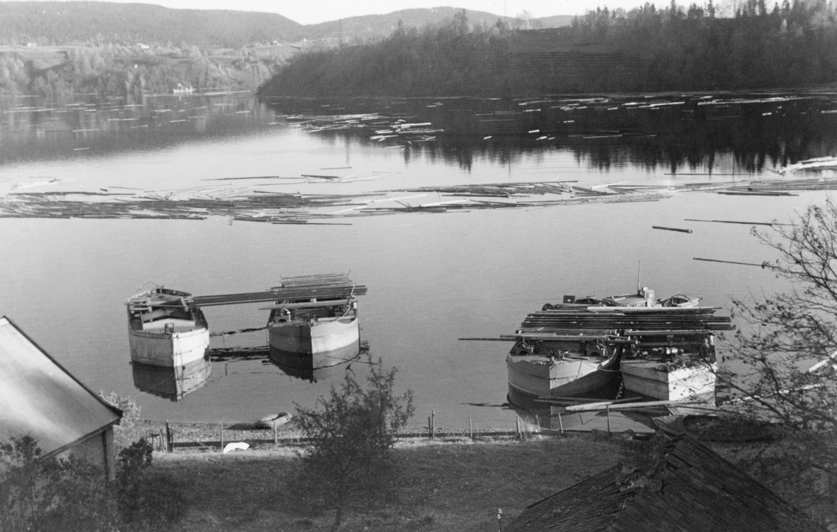 Stemning fra Minnevika, ved Vormas vestre bredd umiddelbart nedenfor Minnesundbrua. I forgrunnen, ved standa, lå det fire stållektere og på vannspeielet i bakgrunnen fløt det en del tømmer. Fotografiet er tatt i begynnelsen av oktober 1940. Dette året ble jernbane- og vegbrua over sundet skadd i forbindelsen med den tyske invasjonen. For å gjøre det mulig for trafikken å passere ble det bygd ei midlertidig trebru - omtalt som pontongbrua - ved siden av. Dette var en lav, delvis flytende konstruksjon, som naturligvis stengte for fløtingstømmeret, som derfor ble liggende lenge på vent i ytterenden av Mjøsa. Først fra midten av september, etter at i hvert fall jernbanetraséen på den egentlige Minnesundbrua var reparert, ble det lagd en åpning i den midlertidige brua, slik at Glomma fellesfløtingsforening kunne få tømmeret fra Mjøsvassdraget fram. I Glomma fellesfløtingsforenings årsrapport for 1940 er dette kommentert slik: «Av de mange vansker som omstendighetene i 1940 medbrakte for fløtningen var sperringen av Mjøsas utløp, hvorved også de båter som skulle anvendes tl fløting innen Mjøsa, ble stengt nede i Vorma. På Mjøsa var vi derfor gjennom hele sommeren henvist til å bruke 2 ganske små leide båter. Sortering og sopping var helt tilendebrakt i begynnelsen av september, men utslepingen kunne ikke ta sin begynnelse før vi den 13. september hadde fått slepebåtene opp fra Vorma,»