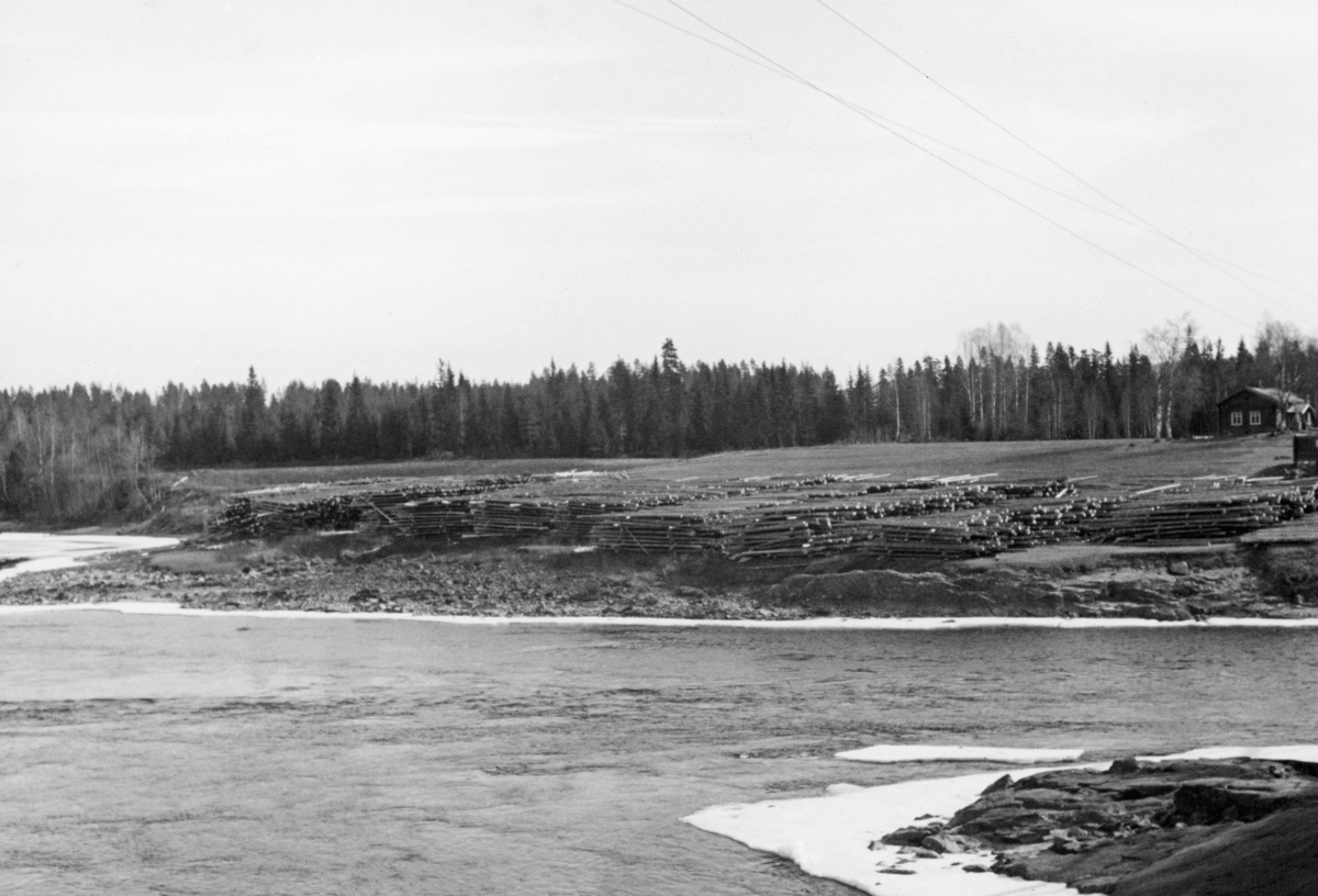 Strøvelter ved Glomma, fotografert 1. mai 1941. Fotografiet er tatt på tvers av elveløpet, mot innmarka på et lite bruk, der arealene mot elva, i hvert fall seint på vinteren og tidlig på våren, var disponert til tillegging av tømmer fra vinterens drifter. I strøveltene nå stokkene tett og parallelt, flovis, vinkelrett på mellomliggende strøstokker som skulle sørge for lufting, slik at tømmeret fikk en forsiktig tørk før det ble slått på elva når fløtingssesongen startet. Ettersom stokkene i floene lå parallelt med elvas strømretning var det vanligvis en enkel sak å rulle tømmeret fra slike velter ned en liten elveskråning slik at stokkene rullet ut i vannet med tyngdekraftas hjelp. Her kan det ha blitt litt vanskelig, for elveskråningen var preget av utrasninger og var følgelig svært ujevn. I bakgrunnen, ved høyre bildekant, skimter vi ei laftet stue, antakelig et våningshus på eiendommen der tømmervelta var plassert.