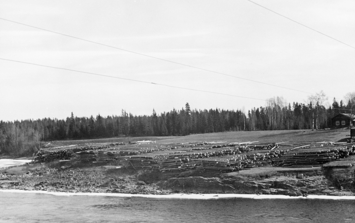 Strøvelter ved Glomma, fotografert 1. mai 1941. Fotografiet er tatt på tvers av elveløpet, mot innmarka på et lite bruk, der arealene mot elva, i hvert fall seint på vinteren og tidlig på våren, var disponert til tillegging av tømmer fra vinterens drifter. I strøveltene nå stokkene tett og parallelt, flovis, vinkelrett på mellomliggende strøstokker som skulle sørge for lufting, slik at tømmeret fikk en forsiktig tørk før det ble slått på elva når fløtingssesongen startet. Ettersom stokkene i floene lå parallelt med elvas strømretning var det vanligvis en enkel sak å rulle tømmeret fra slike velter ned en liten elveskråning slik at stokkene rullet ut i vannet med tyngdekraftas hjelp. Her kan det ha blitt litt vanskelig, for elveskråningen var preget av utrasninger og var følgelig svært ujevn. I bakgrunnen, ved høyre bildekant, skimter vi ei laftet stue, antakelig et våningshus på eiendommen der tømmervelta var plassert.