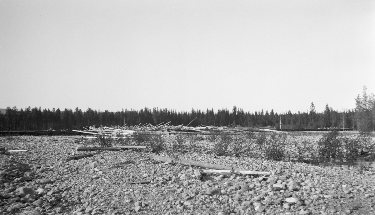 Stor tømmerhaug eller tømmervase i den nedre delen av elva Søndre Osa i Åmot i Hedmark. Dette bildet ble tatt i midten av juni 1932, fra ei kantsone i vassdraget der de finkornete massene var skylt vekk i flomperider, slik at det bare lå småstein igjen på markoverflata. Haugen, som lå i den delen av elvefaret der det fortsatt rant vann, var langstrakt og godt sammenpakket med stokker som sprikte i ulike retninger. Vi kan så vidt skimte fløtere som arbeidet med haker i den ytre enden av haugen (til venstre på dette fotografiet).