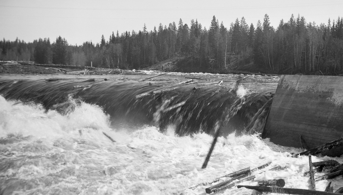 Tømmerfløting i elva Søndre Osa i Åmot kommune i Hedmark. Fotografiet er tatt våren 1936, ved den da nybygde kraftverksdammen ved Kvernfallet. I forgrunnen ser vi hvordan vannet og tømmerstokkene fløt over den avrundete damkrona. Den underliggende konstruksjonen, som vi ikke ser på dette bildet, var utført i armert betong. I 1936 var det innmeldt 383 088 tømmerstokker til fløting fra Osensjøen og tilflytende vassdrag. 28 prosent av stokkene ble levert ved Slemma, 10 prosent ved Nordre Osa, 7 prosent ved Brøa, 13 prosent ved Ena med Ulvsjøvassdraget, 7 prosent ved Tverrena og resten, 35 prosent, ble levert ved Osensjøens strender. Alt dette tømmeret. pluss deler av et kvantum på 72 506 stokker som var levert ved Søndre Osa, skulle passere den nye kraftverksdammen ved Kvernfallet. Aktørene i fløtinga var naturlig nok spente på om dammen kom til å bli et hinder der stokkene satte seg fast på eller like nedenfor dammen. Det skjedde ikke. Kvernfalldammen kom ikke til å skape nevneverdige problemer for tømmerfløtinga.