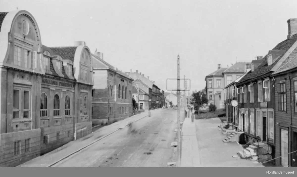 Postkort. Bodø, Storgata østover fra Havnegata. Bebyggelse på begge sider. Tatt litt ovenfra.