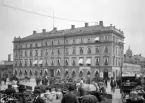 Folkliv på Stora torget i Linköping år 1900. Stora hotellet i fonden stod klart 1852 och var då en av landets första hotellbyggnader. Byggmästaren Jonas Jonssons ursprungliga byggnad var i tre plan, den fjärde våningen tillkom 1892-93 efter ritningar av Adolf Emil Melander. Redan från invigningen drevs butiker i hotellets markplan. Närmast kameran siktas familjen Brobecks manufakturaffär.