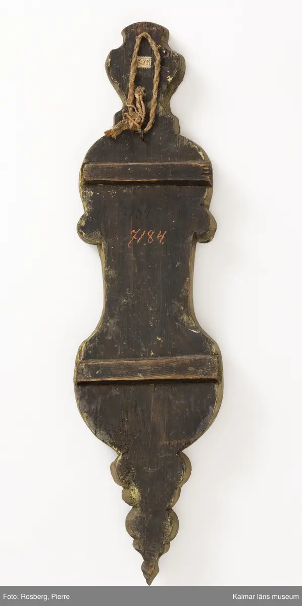 KLM 7184. Lampett, spegellampett. Av trä, bly och spegelglas. Flera utbuktningar, fiolformad, kurvig i flera avdelningar. Väggskivan med profilerad kant, belagd med fyra spegelskivor, fästa med blyram. Väggskivan/bakstycket av trä med förgyllda kanter. Två av spegelskivorna med 8-uddiga stjärnor och en enkel rund figur. Avsedd för en ljushållare, infästning av metall.