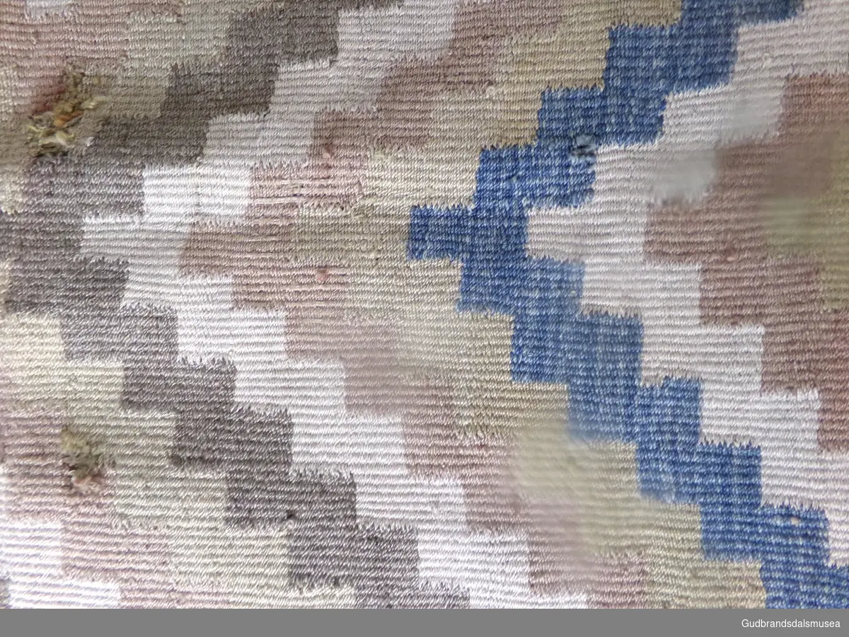 Åkle med rutemønster og striper i begge ender, ellers et teppemønster som går sammen i en stor X. Rutesmett.
Fargene er brun, beige, gul, rødbrun og med innslag i grovt ullgarn (2 tråds grov lin). Kjerringtann (påteskaft)
Åkleet er avklippet i en ende.