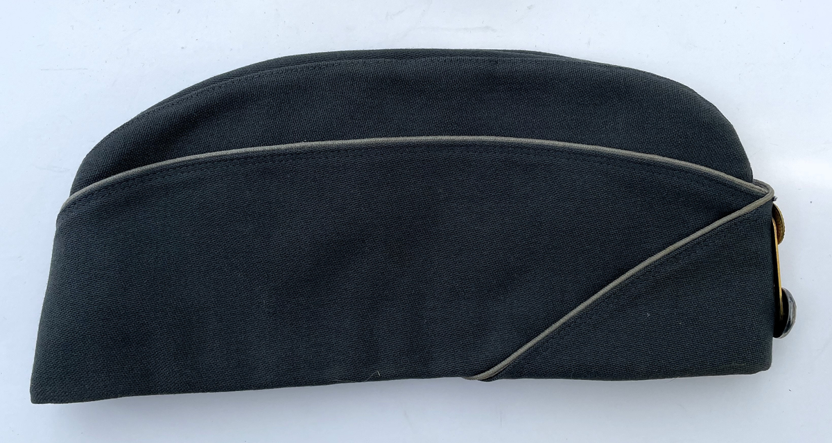 Stålgrå vintermössa m/1960 med gråblå passpoal. Agraff i guld.  Knapp för underofficer m/1865-1960. Vintermössa m/1960 är i samma utförande som Båtmössa m/1960, men har öronskydd och vaddstickat foder.
