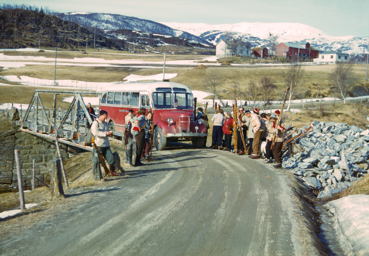 Leirfjord, Meisfjord (Simsødalen). Folk som har kommet med buss fra Sandnessjøen for å gå på skitur i Leirfjord, Simsødalen. Her er folk med ski, kledd i turutstyr som anorakker, strikkegensere, og ryggsekker. På bussen, en Volvo, står det "Leirfjord - "Sandnessjøen". Volvomodellen var populært kalt "Rundnos/Rundnese" etter formen på snuten. Denne typen buss ble hovedsakelig produsert 1946-1953.
Bildet er brukt i Leirfjordkalenderen - desember 2024.