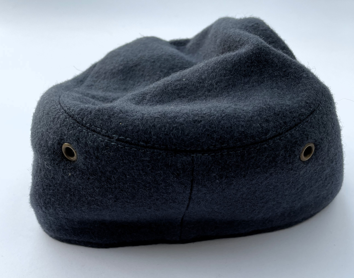 Mörkt blågrå Vintermössa m/1950-1960 i kläde. Modell som vintermössa m/1950. Nationalitetsmärke m/1941 och små knappar m/1939-1960 i guld.