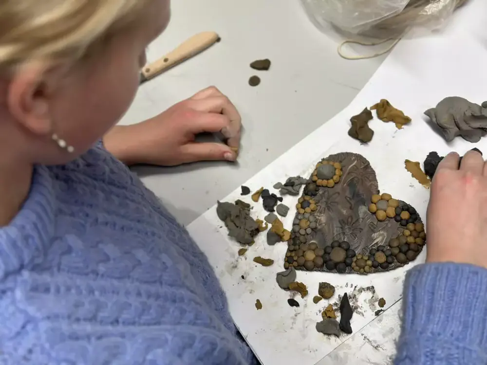 Et barn iført en blå strikkegenser deltar i en verkstedsaktivitet på Norsk Maritimt Museum. Barnet lager et hjerte av leire.