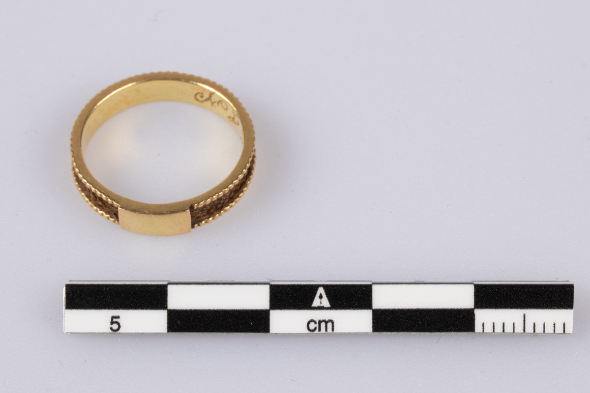 18 karats gullring med flettet hår rundt yttersiden av ringen. På innsiden er der et legeringsstempel og inngravert monogram