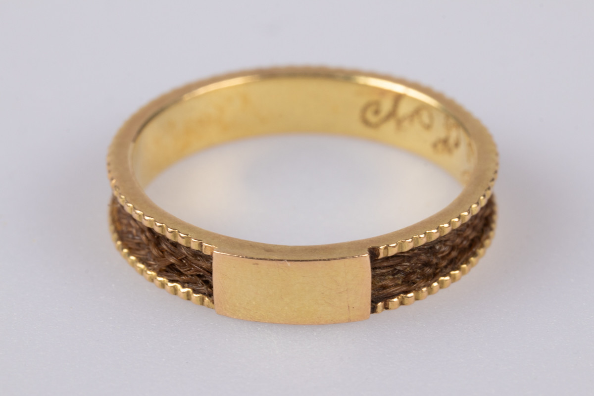 18 karats gullring med flettet hår rundt yttersiden av ringen. På innsiden er der et legeringsstempel og inngravert monogram