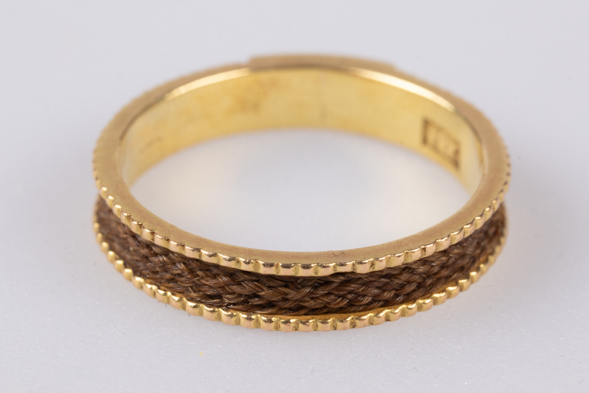 18 karats gullring med flettet hår rundt yttersiden av ringen. På innsiden er der et legeringsstempel og inngravert monogram