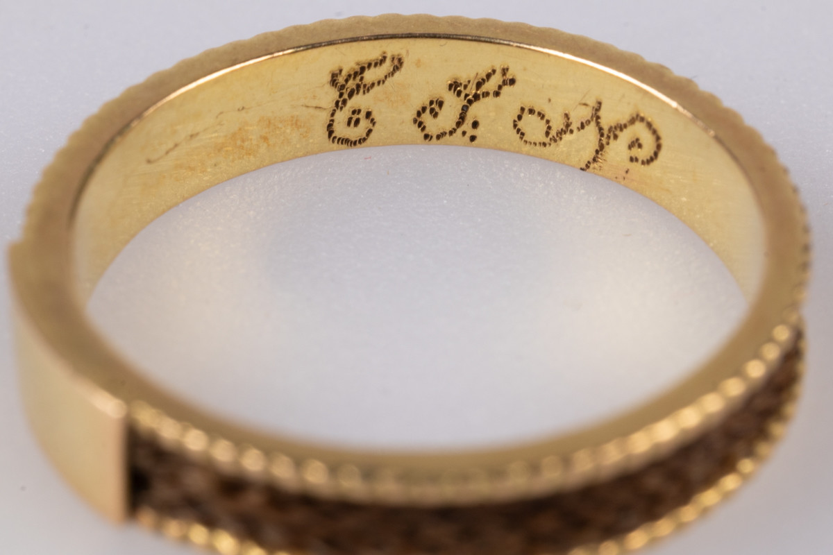 18 karats gullring med flettet hår rundt yttersiden av ringen. På innsiden er der et legeringsstempel og inngravert monogram