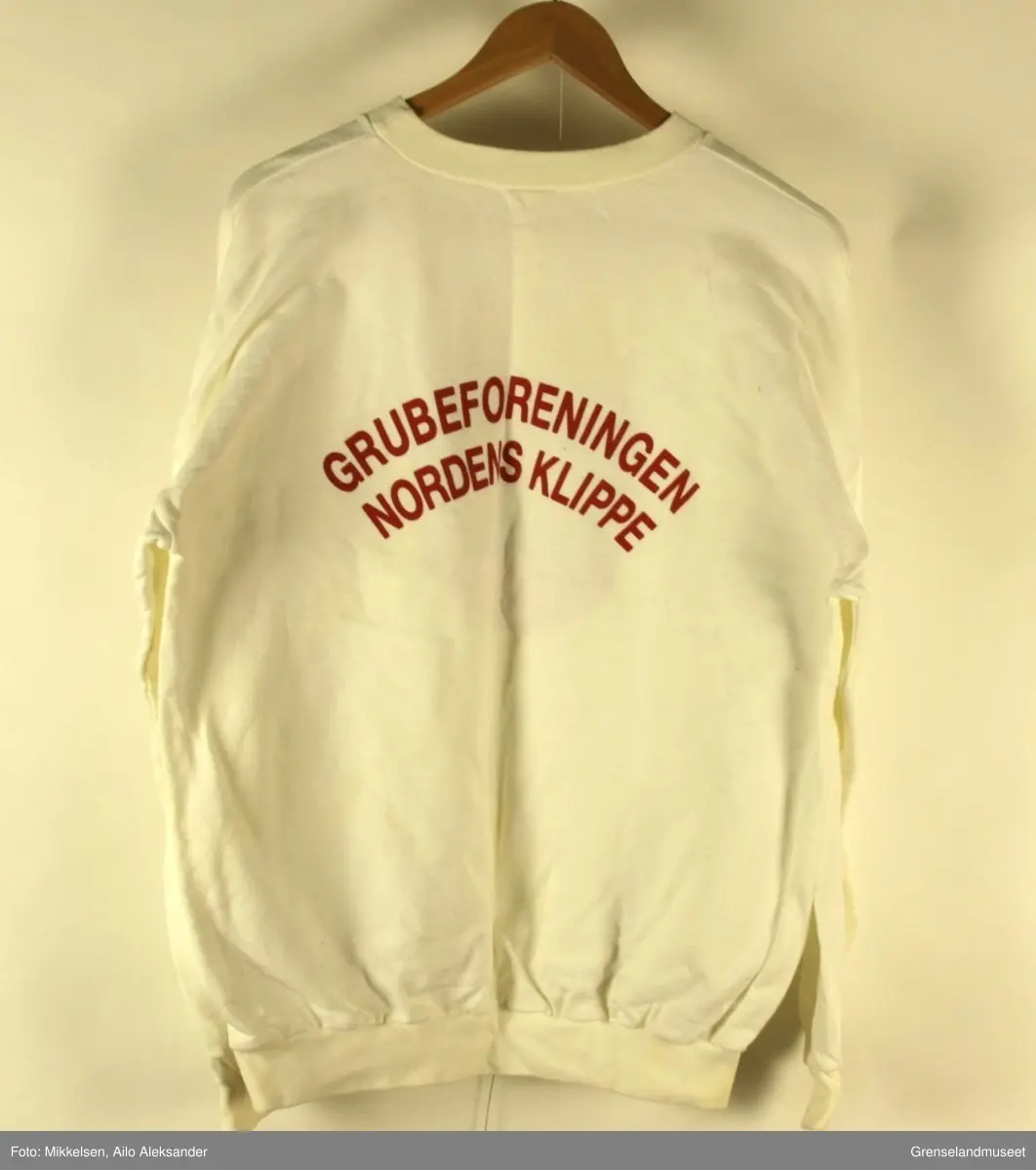 En langarmet hvit genser med logoen til Grubeforeningen Nordens Klippe på forsiden og på ryggen i rød skrift "Grubeforeningen Nordens Klippe".