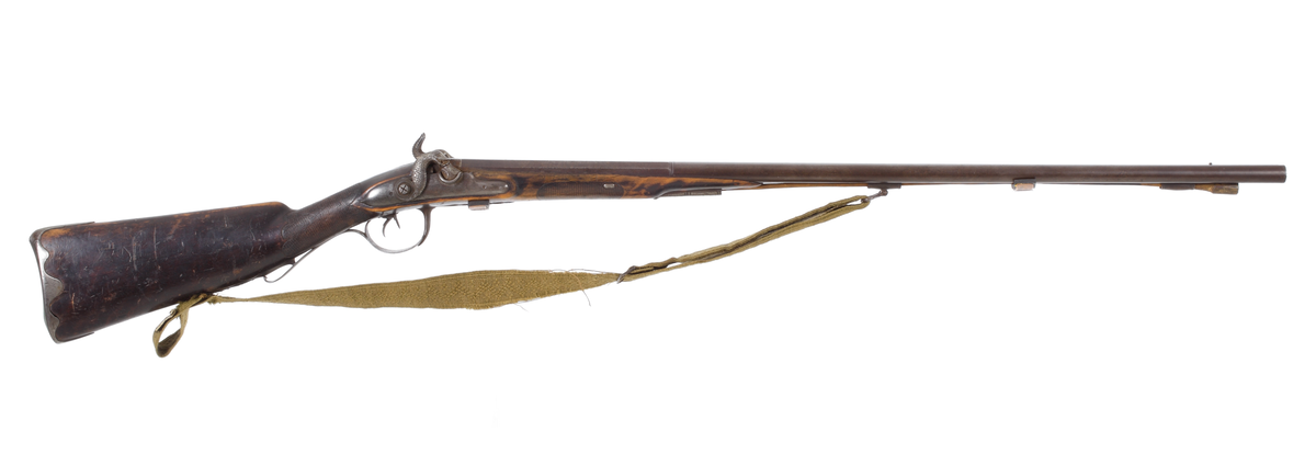 Dubbelpipigt jaktgevär ombyggt från flintlås till slaglås. Låsblecken är kullriga och har varit blankpolerade. Hanarna på vardera sidorna är formade som fiskar. Piporna är runda med en åttakantig avslutning bak mot hanarna. Kolven är slät och har ett kindstöd på vänster sida. Bakplåten är av stål och omsluter kolvens bakkant, som även går upp en bit på kolvryggen. Kolvhals och framstock är delvis rutade. Laddstocken sitter i tre rörkor, och vid den mellersta finns bärremmen infäst med en bygel. Bärremmens andra ände sitter fästad i kolvens underkant med hjälp av en bred skruv. Geväret har ett gropsikte placerat mellan hanarna, och sju centimeter bakom mynningarna, mellan piporna, sitter kornet bestående av en stålknapp. Piporna är slätborrade med en innderdiameter på 16 mm. Bärremmen är en vävd textil i olivgrön nyans.
Inskrivet i huvudkatalog 1892-1900.