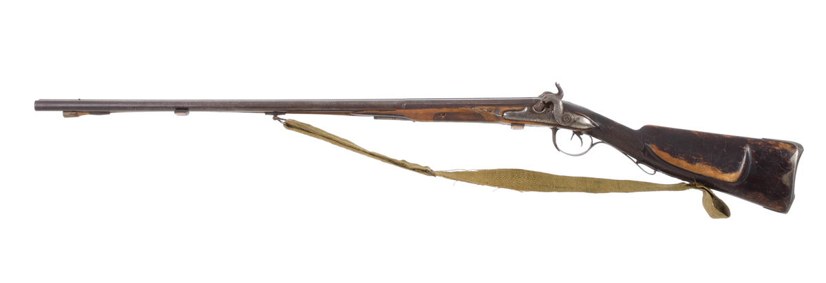 Dubbelpipigt jaktgevär ombyggt från flintlås till slaglås. Låsblecken är kullriga och har varit blankpolerade. Hanarna på vardera sidorna är formade som fiskar. Piporna är runda med en åttakantig avslutning bak mot hanarna. Kolven är slät och har ett kindstöd på vänster sida. Bakplåten är av stål och omsluter kolvens bakkant, som även går upp en bit på kolvryggen. Kolvhals och framstock är delvis rutade. Laddstocken sitter i tre rörkor, och vid den mellersta finns bärremmen infäst med en bygel. Bärremmens andra ände sitter fästad i kolvens underkant med hjälp av en bred skruv. Geväret har ett gropsikte placerat mellan hanarna, och sju centimeter bakom mynningarna, mellan piporna, sitter kornet bestående av en stålknapp. Piporna är slätborrade med en innderdiameter på 16 mm. Bärremmen är en vävd textil i olivgrön nyans.
Inskrivet i huvudkatalog 1892-1900.
