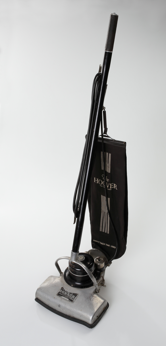 Elektrisk dammsugare av märket The Hoover, tillverkad i USA mellan åren 1923-25. Dammsugaren består av ett sugmunstycke på fyra mindre hjul och med roterande borste. Motorn är placerad ovanpå munstycket. Från sugmunstycket leder ett fällbart/ledat skaft samt en monterad textil dammsugarpåse som går att lossa och haka av vid tömning.